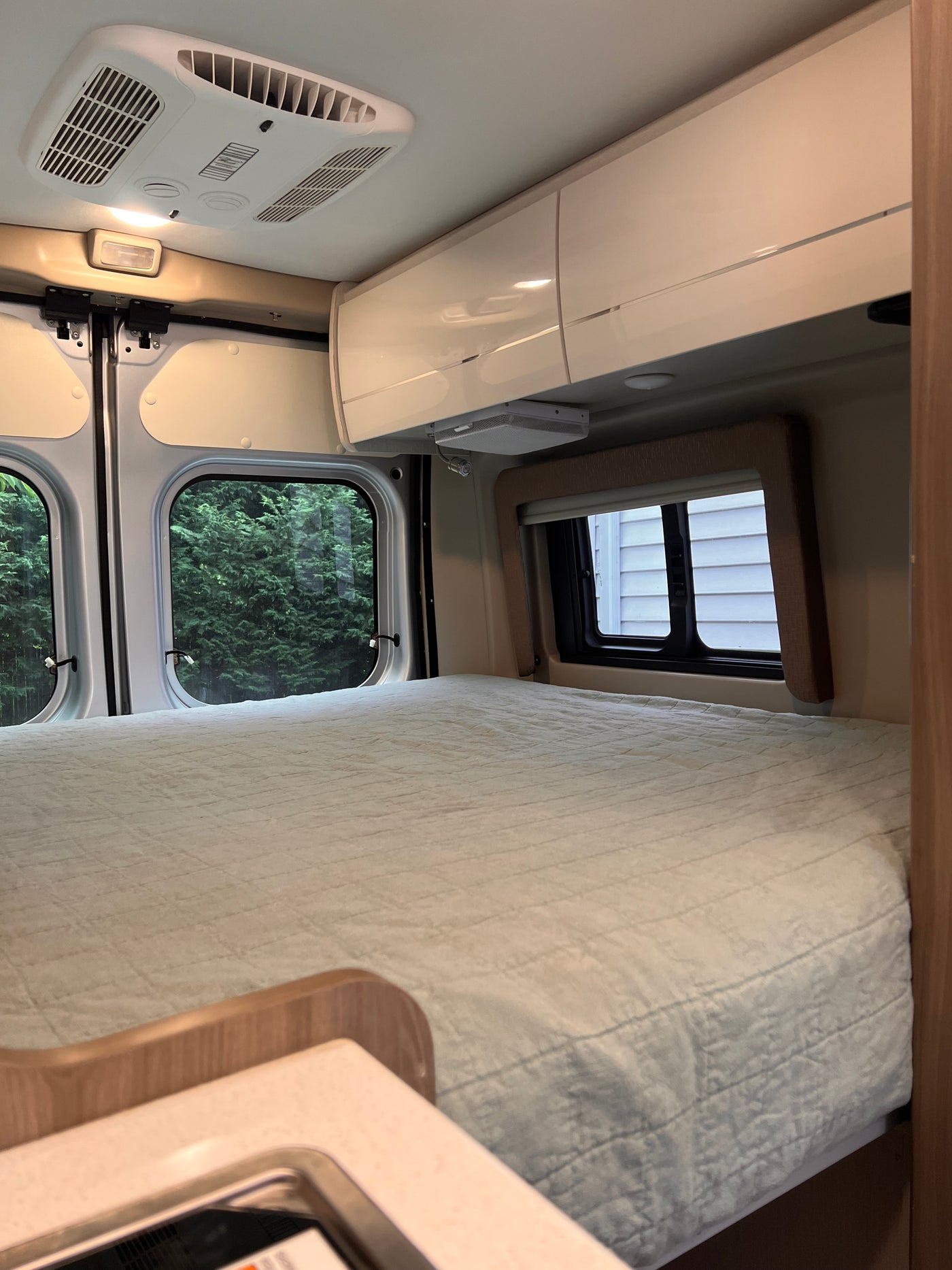 Cozy RV rental sleeping area with comfy bed, windows showing trees, AC, and overhead cabinets for travel comfort. — photo 6