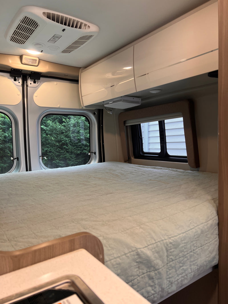 Cozy RV rental sleeping area with comfy bed, windows showing trees, AC, and overhead cabinets for travel comfort. — photo 6