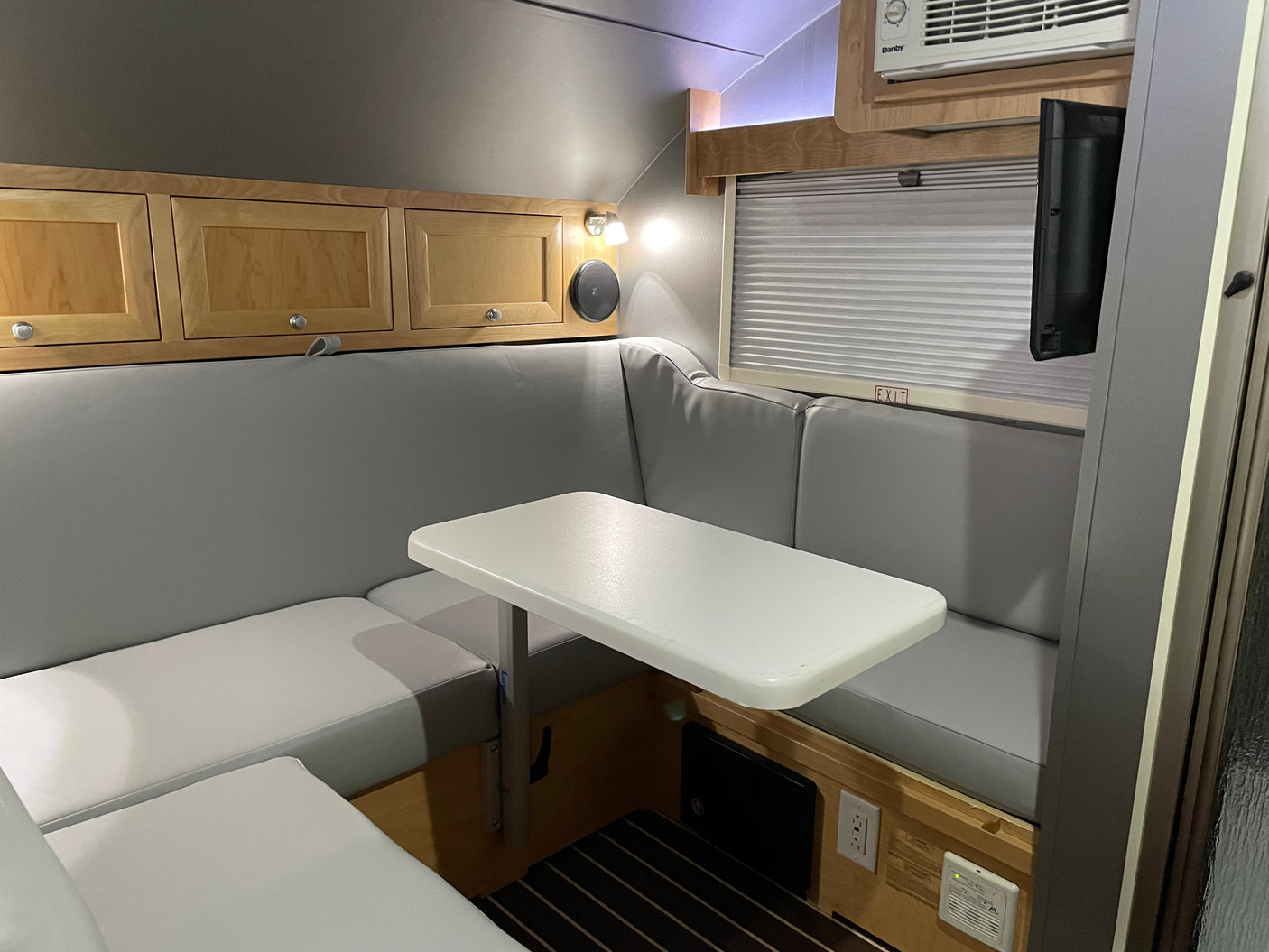 Cozy RV rental dinette area featuring U-shaped seating, table, overhead cabinets, TV, and AC unit.