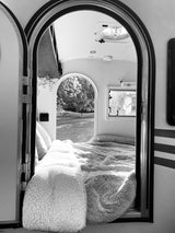 Cozy RV rental interior with bed & a view of nature through the arched doorway. Perfect for a relaxing travel escape.