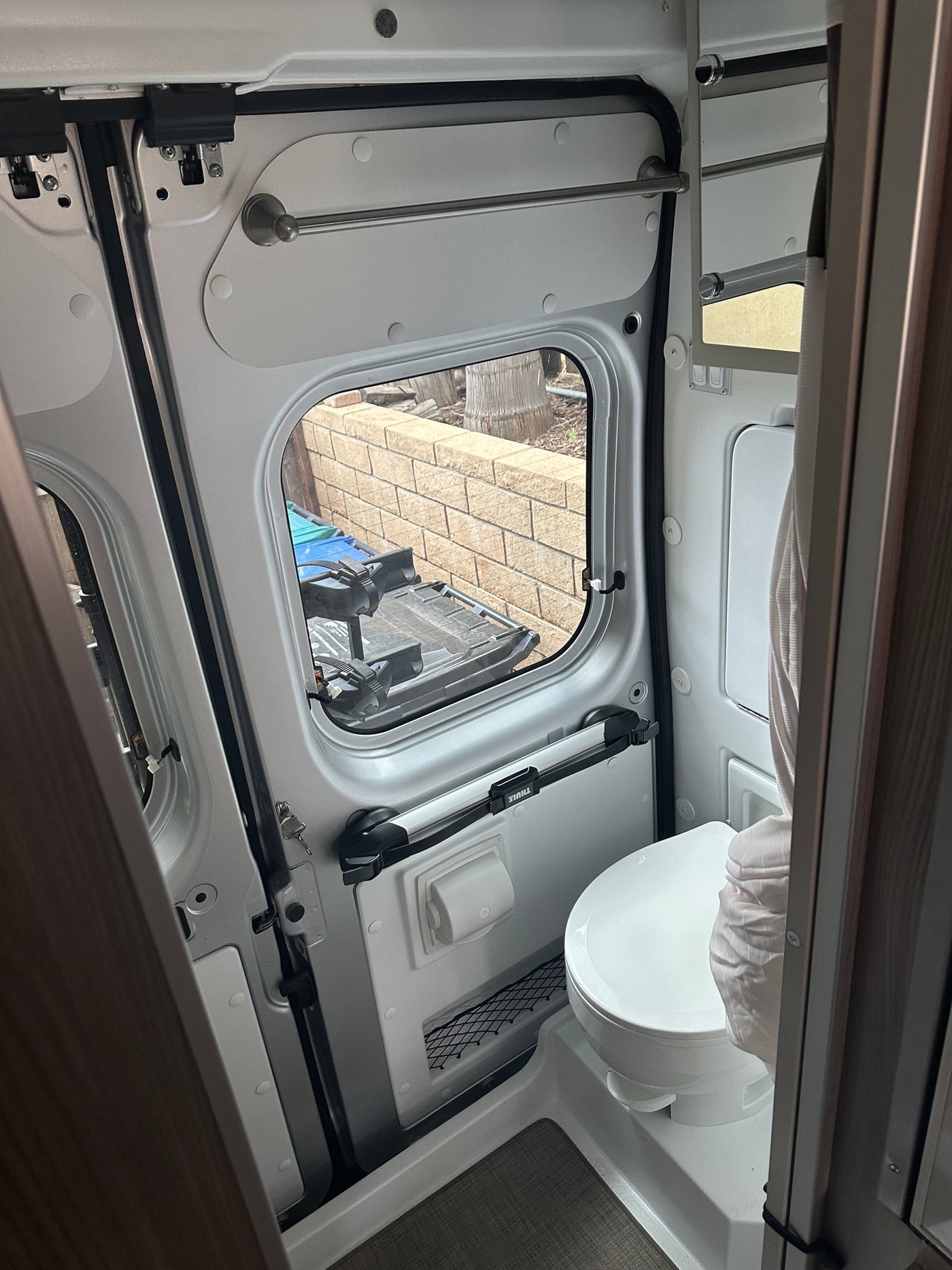 Compact RV rental camper van bathroom with a toilet, window, and wall-mounted storage including a towel bar. — photo 15