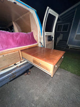 Explore the convenience of an RV rental: a custom camper van with a cozy bed and an extendable outdoor kitchen/table.