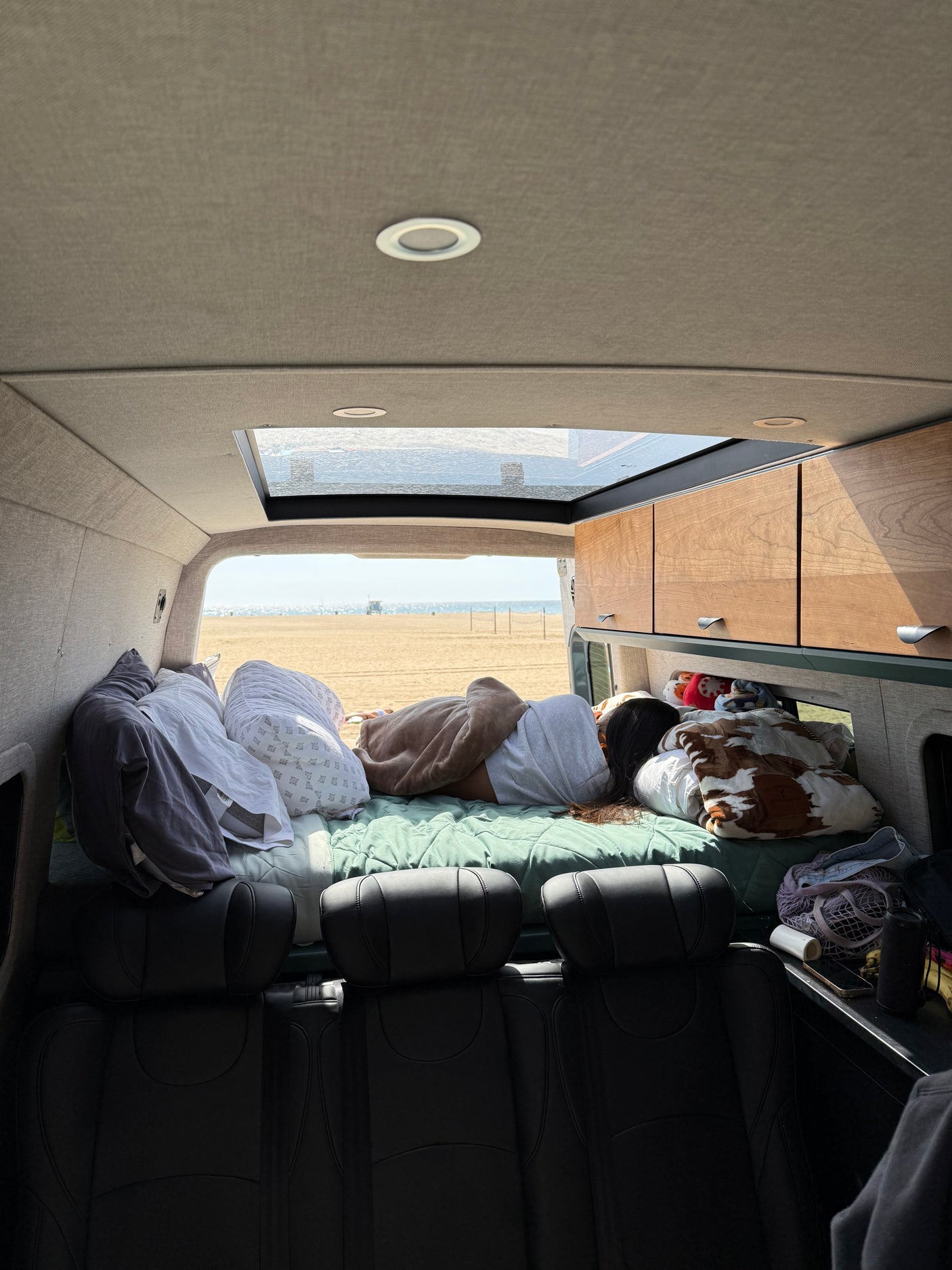 RV rental: Relaxing nap in a camper van overlooking a serene beach. Perfect beach day comfort.
