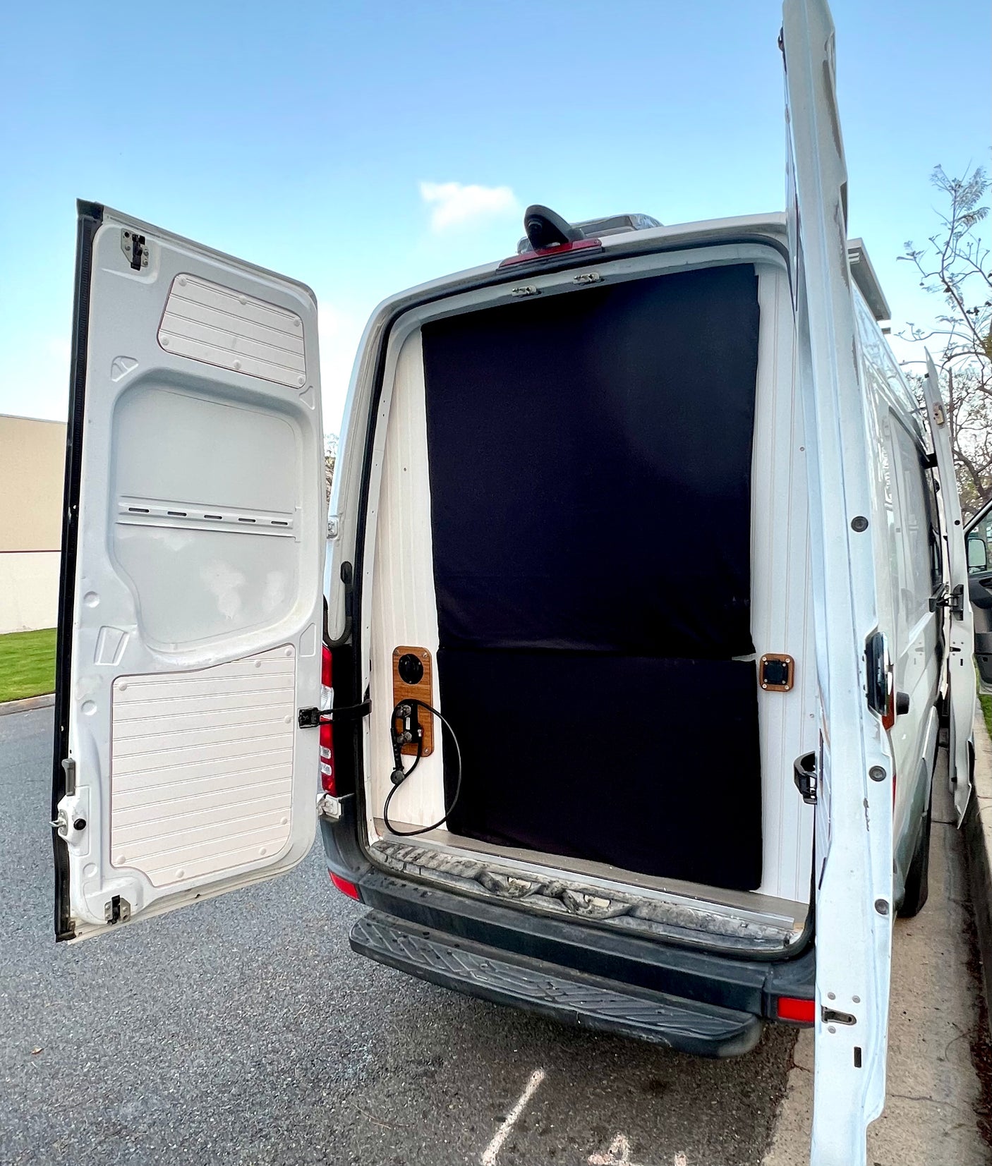 Rear of an RV rental camper van with doors open, showing an interior privacy curtain & power outlet. Ready for trips!
