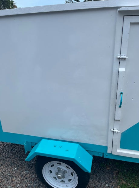 Side view of a white and teal utility trailer with a side door and wheel, a versatile option for RV rental services.
