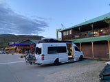 This RV rental Sprinter van with bikes is parked with its door open in a scenic mountain town.