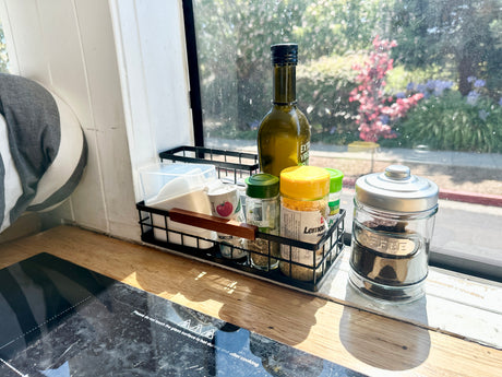 Inside an RV rental: a neat kitchen setup with spices, olive oil, coffee, and an induction cooktop by a sunny window.