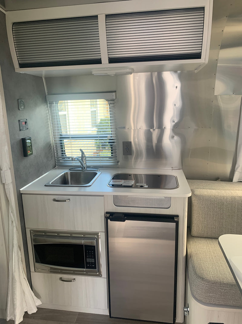 Modern RV rental interior showcasing a compact kitchen with sink, stovetop, microwave, fridge, and adjacent dinette. — photo 9