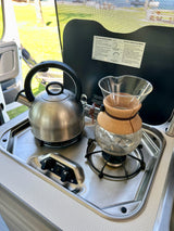Inside an RV rental: a compact kitchen with a two-burner stove, kettle, and pour-over coffee maker.