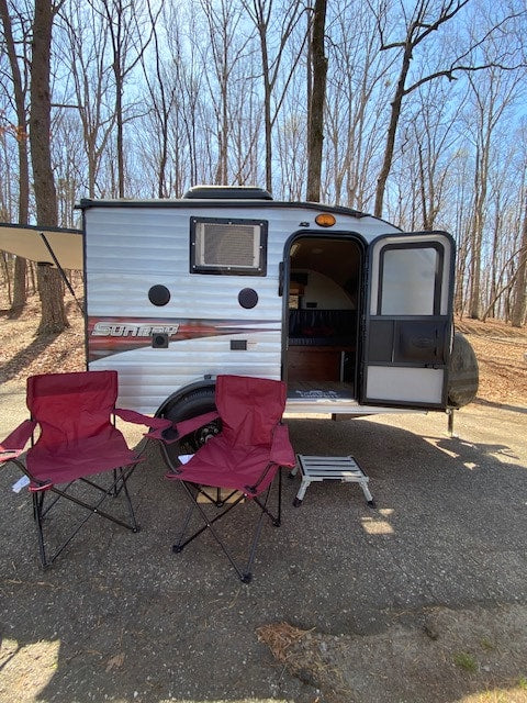  ideal for camping.|Exploring nature with our RV rental. A small dog sits in the doorway of a silver Sunray camper at a campsite.|A small RV rental travel trailer is parked at a campsite