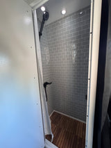RV rental's modern shower features gray subway tiles, a wooden slatted floor, and black fixtures.