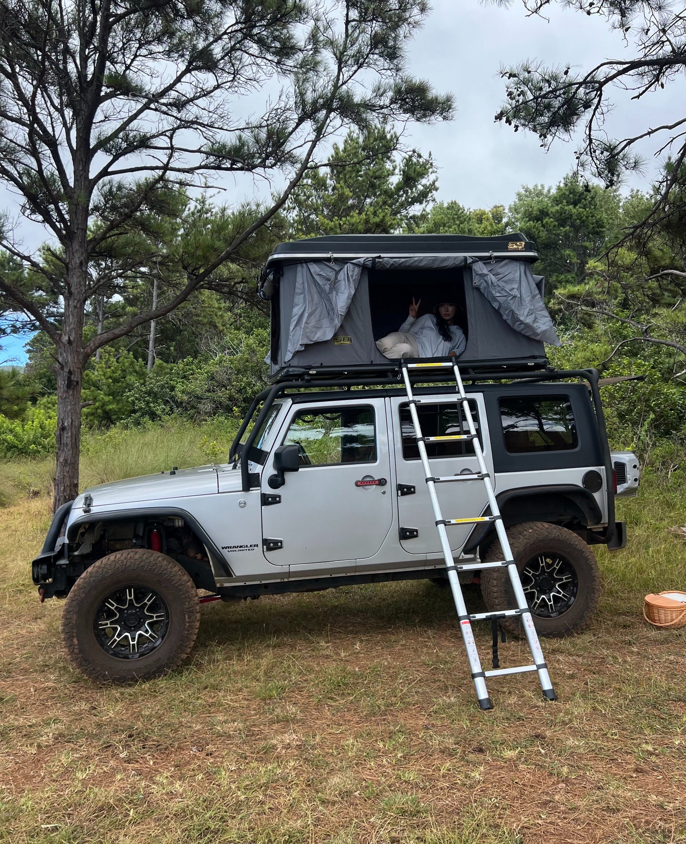 RV rental adventure awaits! A person relaxes in a rooftop tent on a Jeep Wrangler, ideal for outdoor camping escapades.
