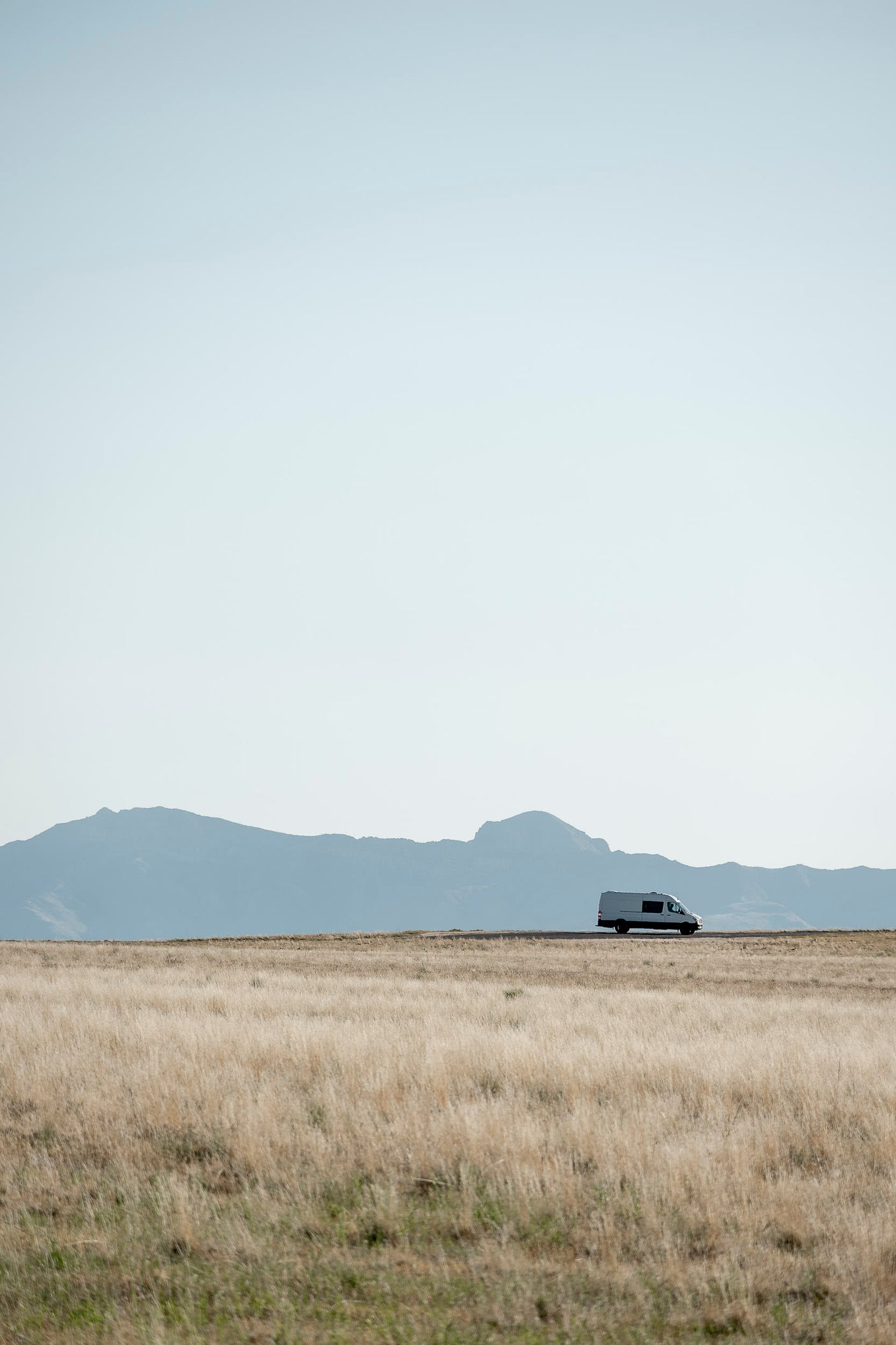 An RV rental drives past vast golden fields with distant blue mountains under a bright sky, perfect for exploring.