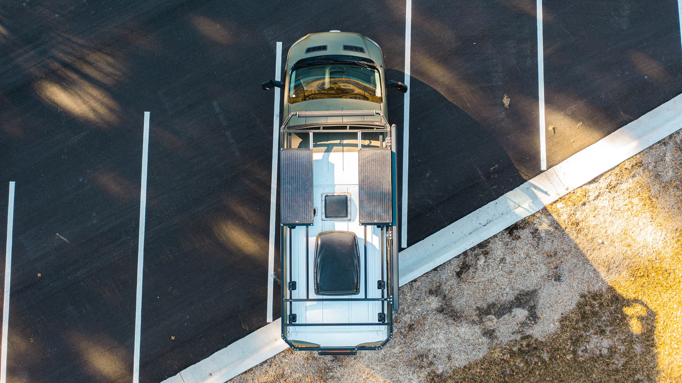 Aerial view of a sleek RV rental camper van with solar panels parked in a sunny lot, ready for your next trip.