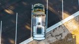 Aerial view of a sleek RV rental camper van with solar panels parked in a sunny lot, ready for your next trip.