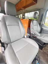 Inside a comfy RV rental: light gray front seats, wooden storage cabinets, and a compact kitchen area.