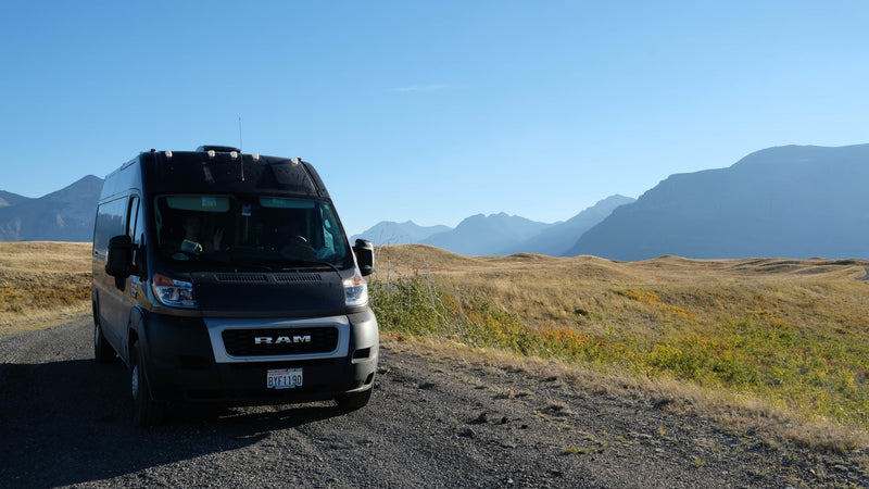 Black RAM camper van, possibly an RV rental, on a gravel road. Panoramic views of mountains & golden hills under a clear sky. — photo 14