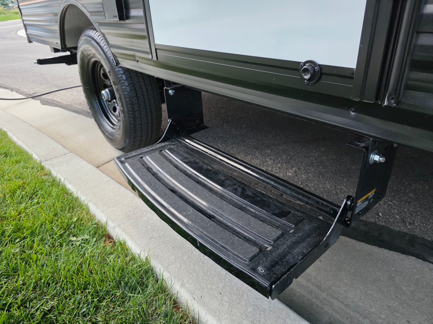 RV rental: Extendable step provides easy entry to this parked camper, seen with its tire by a curb and grass.