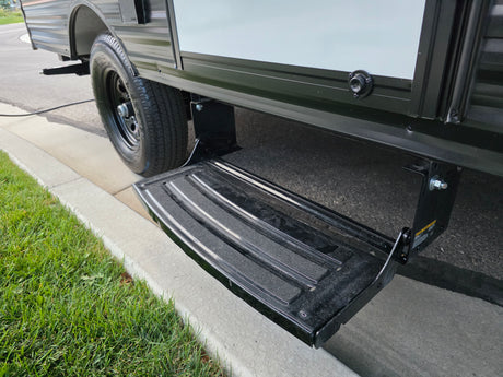 RV rental: Extendable step provides easy entry to this parked camper, seen with its tire by a curb and grass.