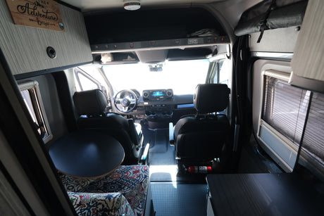 rv rental: Inside a Mercedes-Benz Sprinter camper van, looking forward. Features swivel seats, dashboard, and integrated living space.