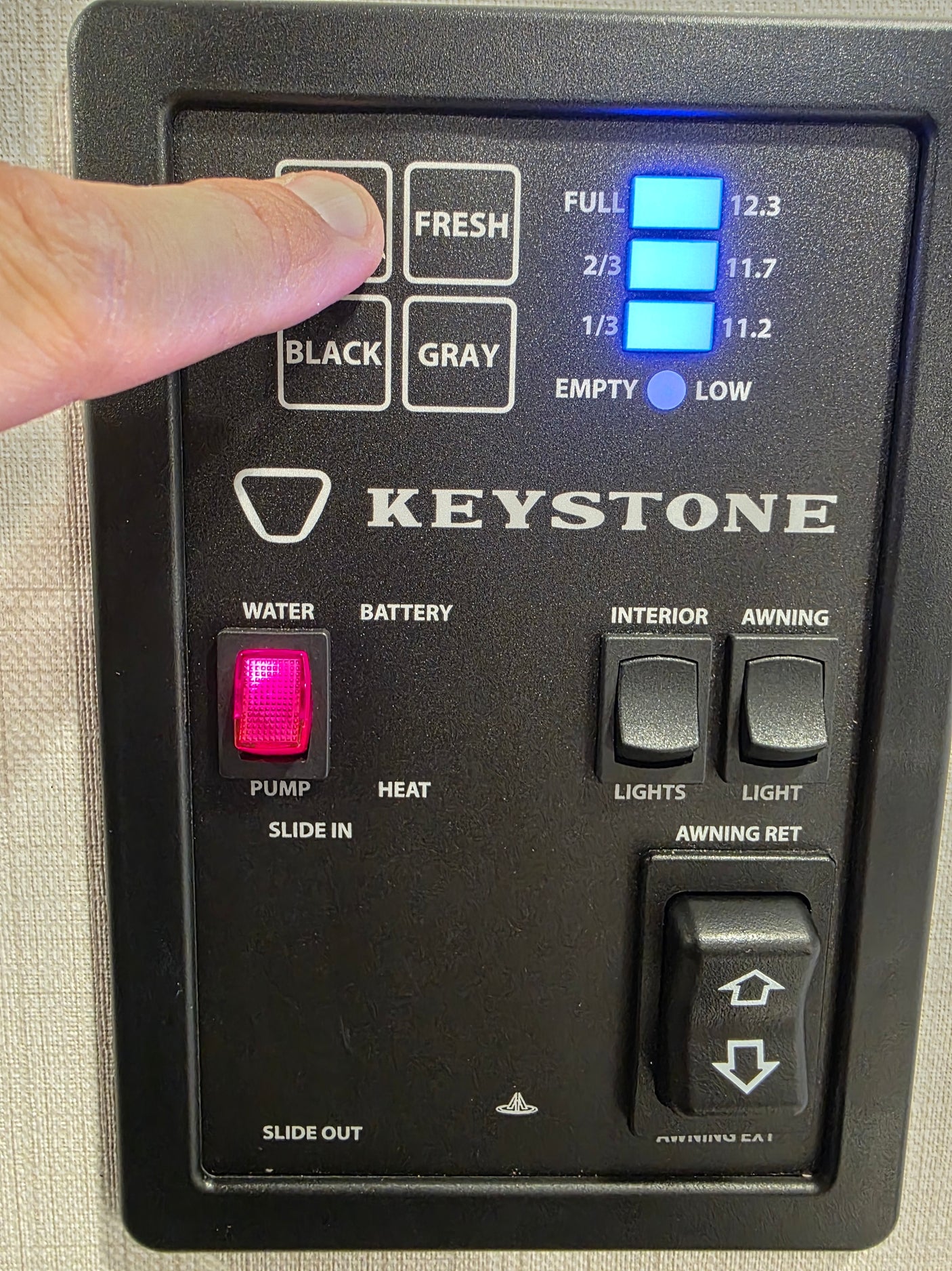 RV rental control panel. Finger checks Fresh water tank, displaying full. Features water pump, lights, awning, and slide controls.