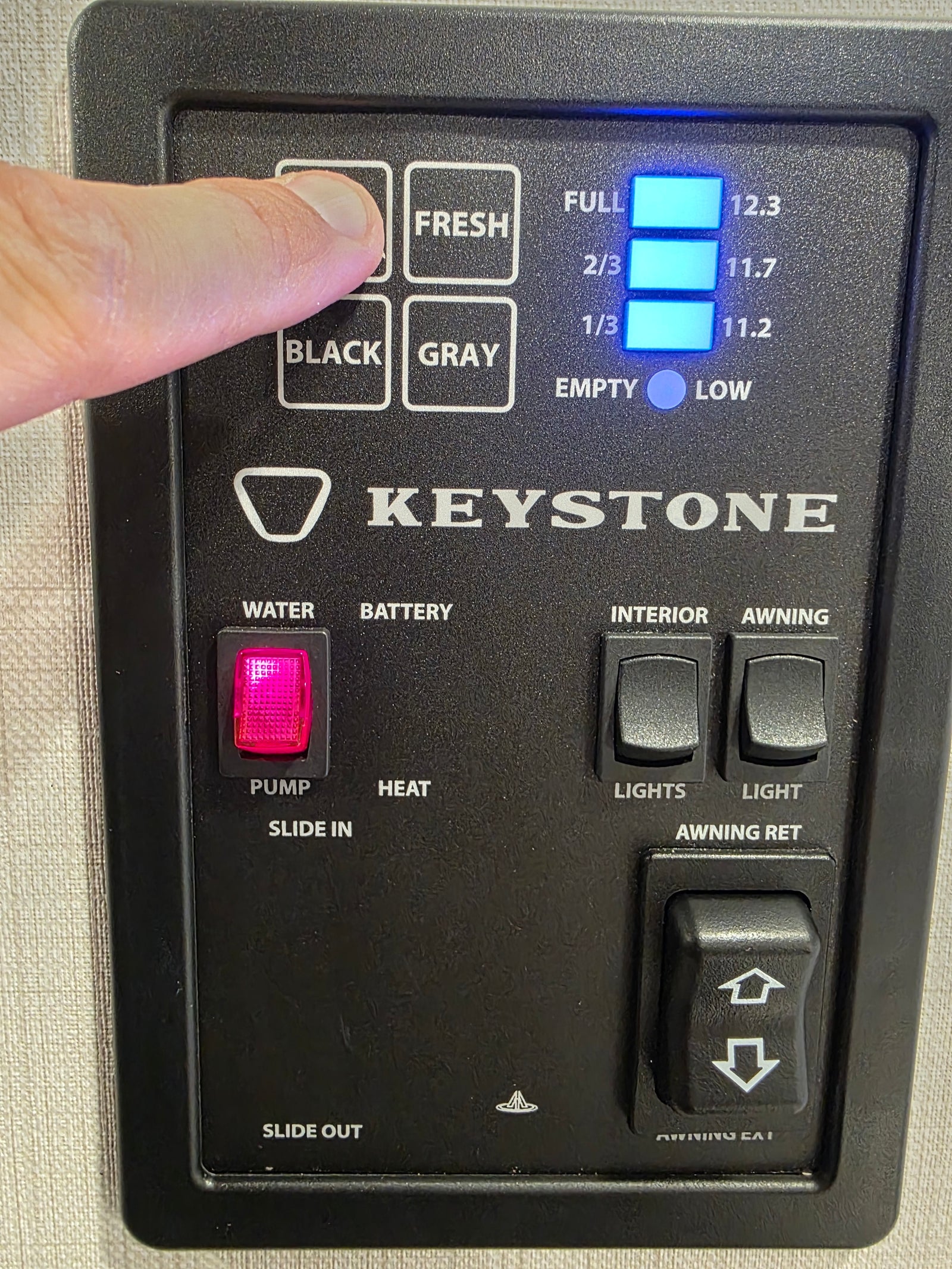 RV rental control panel. Finger checks Fresh water tank, displaying full. Features water pump, lights, awning, and slide controls.