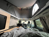 Bright RV rental camper van interior: pop-top roof, cozy bed, and functional kitchen space.