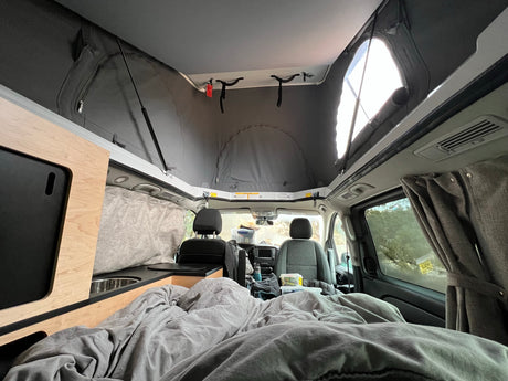 Bright RV rental camper van interior: pop-top roof, cozy bed, and functional kitchen space.