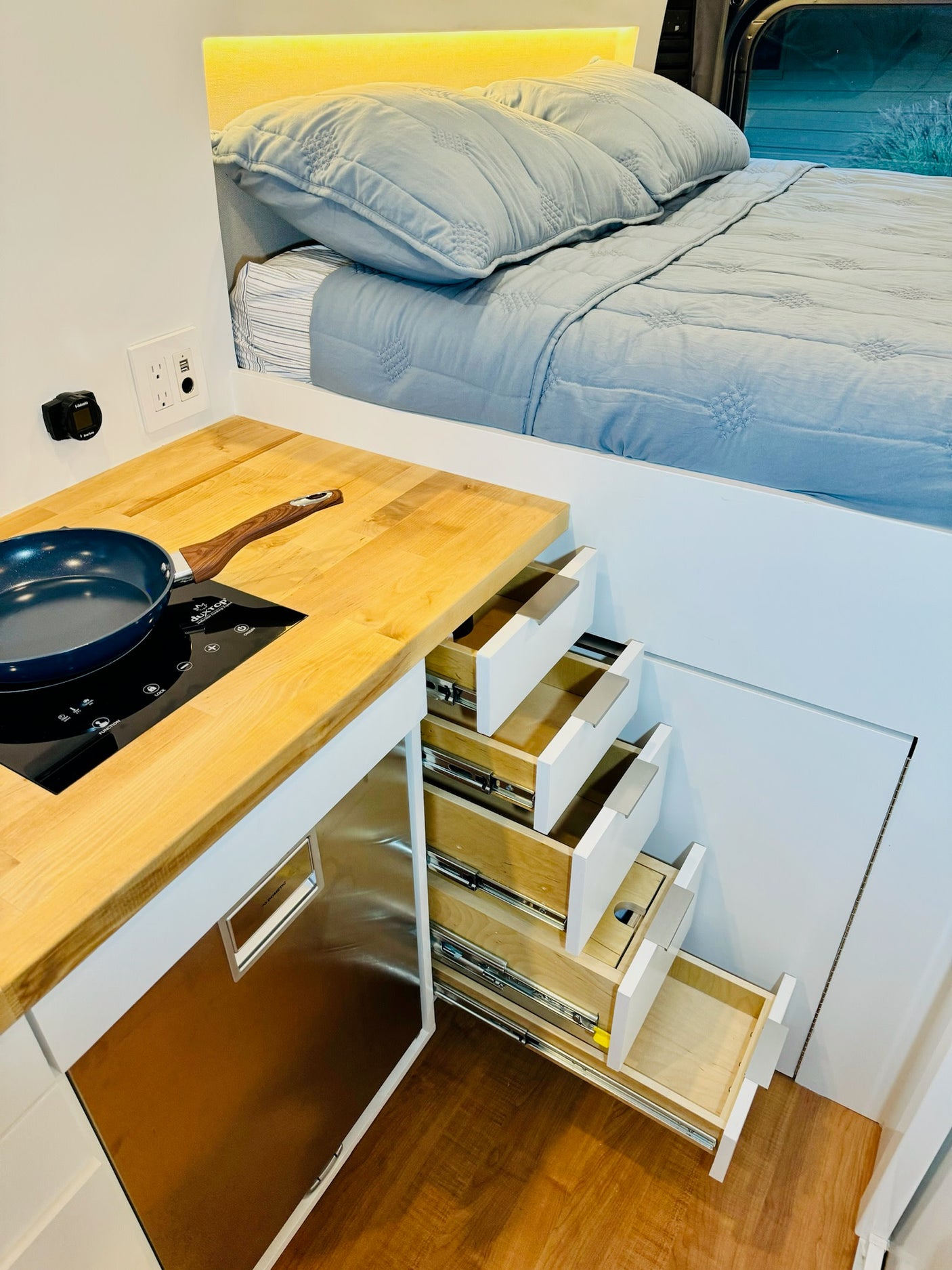 RV rental interior shows a cozy bed, compact kitchen with induction cooktop, and space-saving drawer stairs.