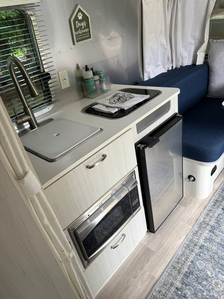 Functional RV rental kitchen with sink, stovetop, microwave, fridge, and blue dinette seating, plus dog decor.