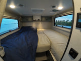 Enjoy the cozy sleeping area inside an **rv rental**, featuring two beds, overhead storage, and scenic window views.