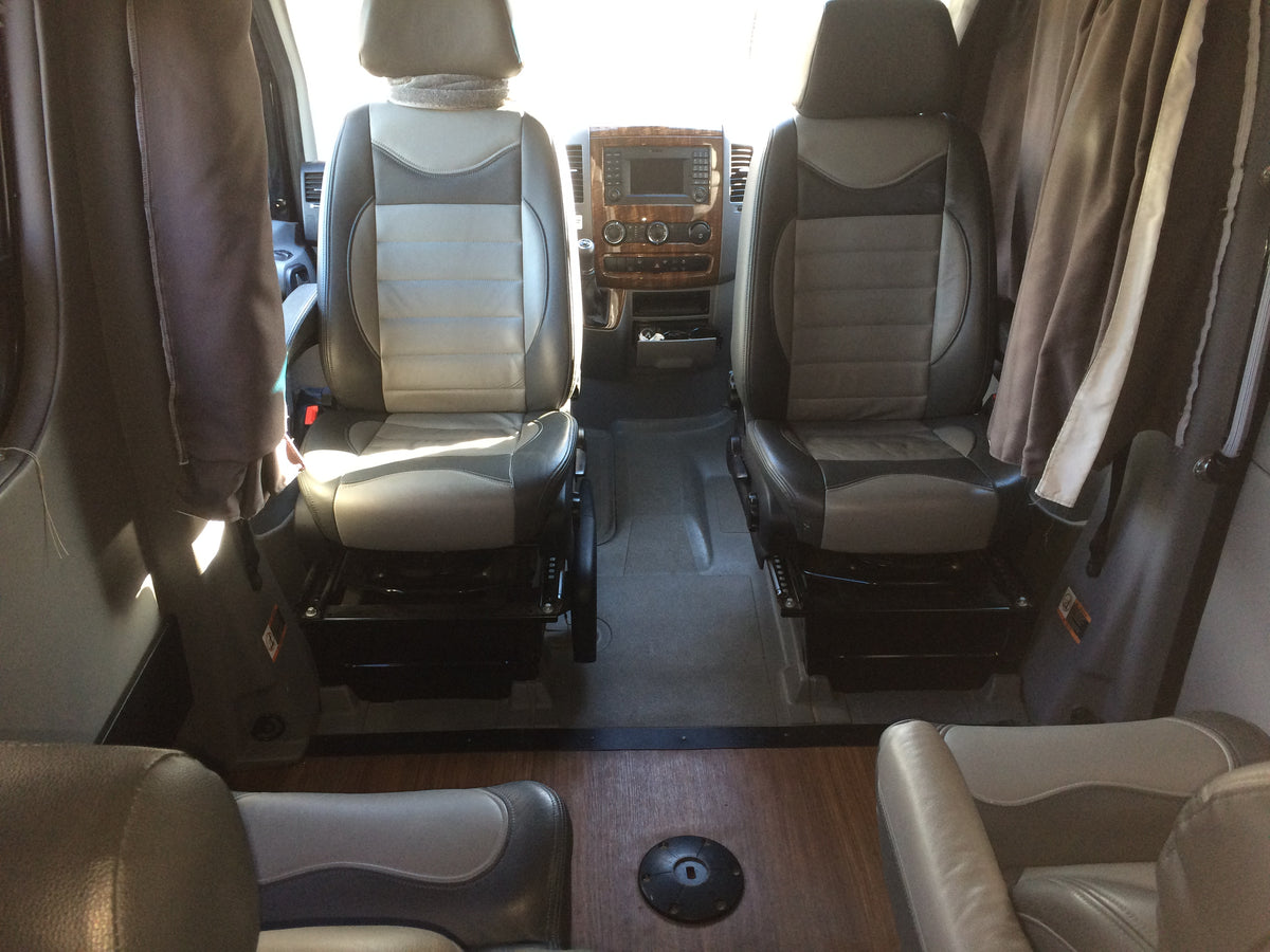 Interior view of an RV rental showing swiveling captain's chairs, dashboard with wood trim, and living area flooring. — photo 10