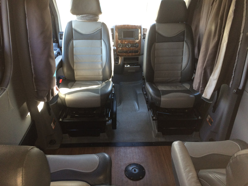 Interior view of an RV rental showing swiveling captain's chairs, dashboard with wood trim, and living area flooring. — photo 10