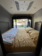 RV rental interior with a cozy bed, AC, and a view of a residential street from the back of the camper van.