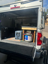 Inside a DIY truck camper, featuring a cooler, propane tank, and bed, offering a cozy alternative to an RV rental.