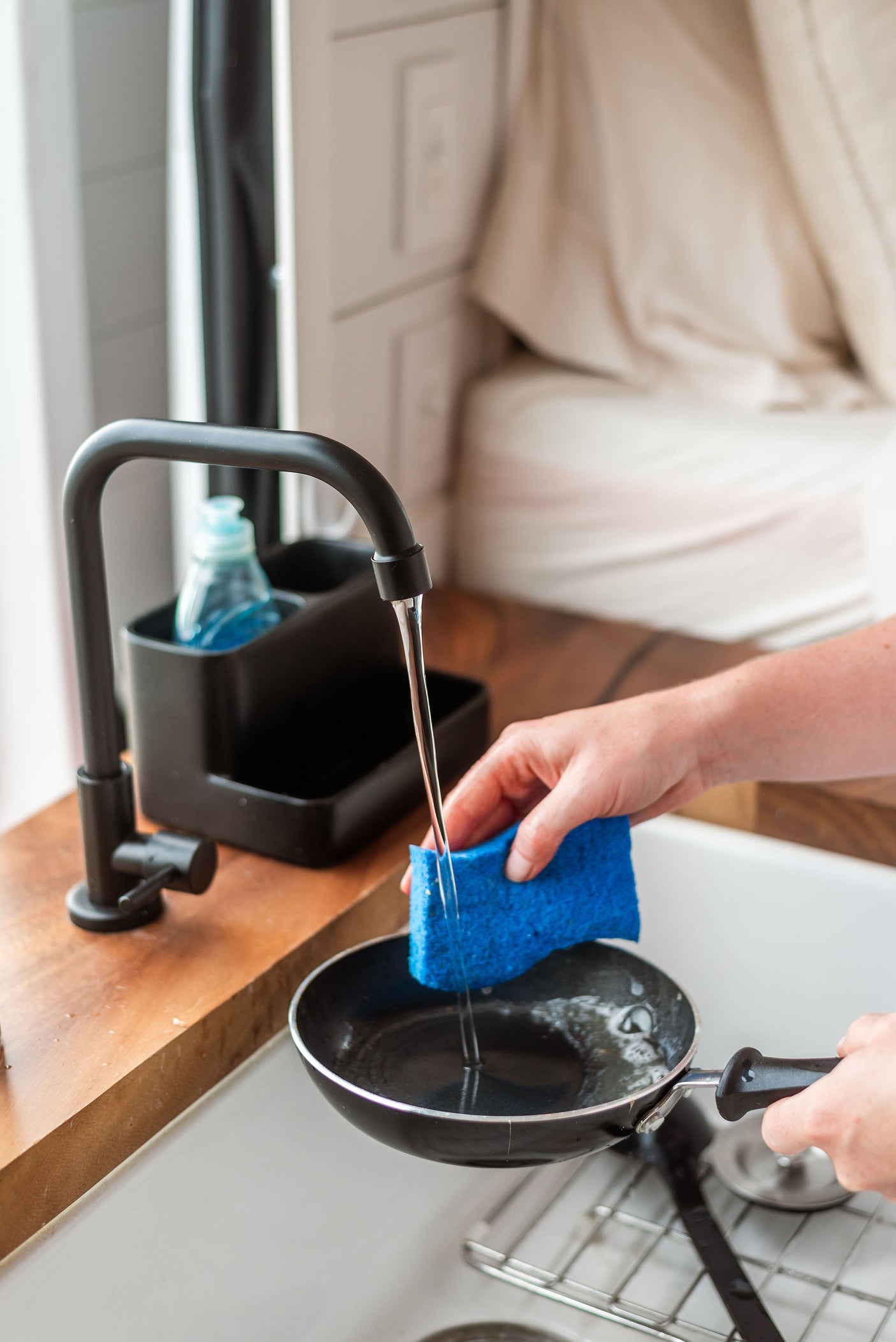 Washing a pan in a compact RV rental kitchen sink. A person uses a blue sponge under running water from a black faucet.