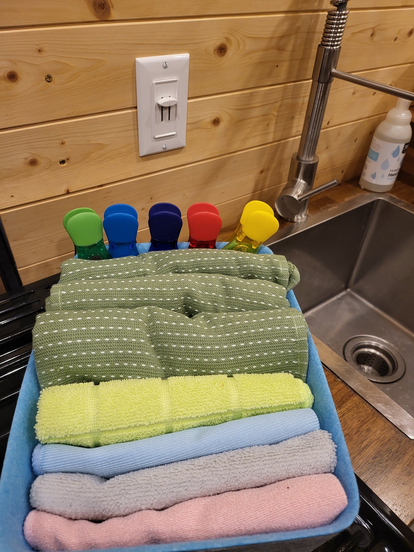 RV rental kitchen showing sink, faucet, soap, and a caddy filled with colorful, neatly rolled towels and clips.
