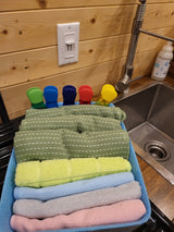 RV rental kitchen showing sink, faucet, soap, and a caddy filled with colorful, neatly rolled towels and clips.