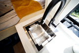 Modern RV rental interior with a sleek kitchen sink, colander insert, and black faucet next to a cozy bed setup.