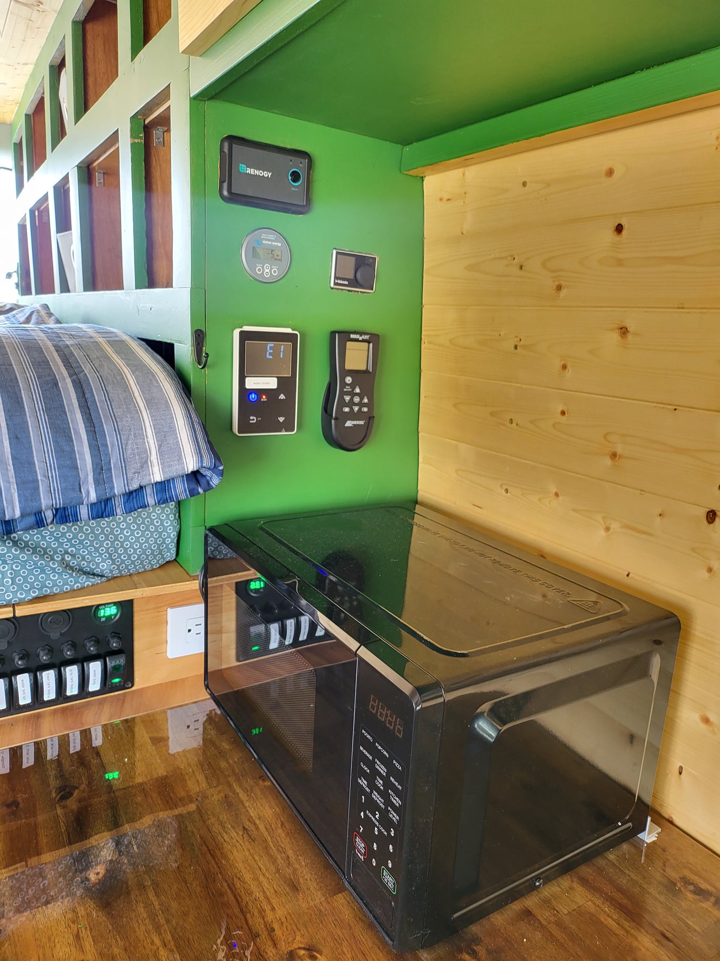 RV rental interior: compact kitchen/utility area with microwave, Renogy, Victron, and other system controls mounted on a green panel.