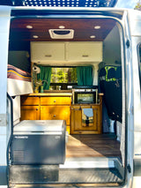 This RV rental showcases a cozy camper van interior with a kitchen, bed, Dometic fridge, and wood cabinets, perfect for van life adventures.