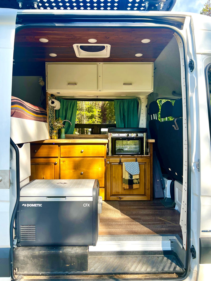 This RV rental showcases a cozy camper van interior with a kitchen, bed, Dometic fridge, and wood cabinets, perfect for van life adventures. — photo 6