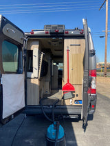 Rear view of an RV rental camper van with open doors, revealing its organized interior, being cleaned.