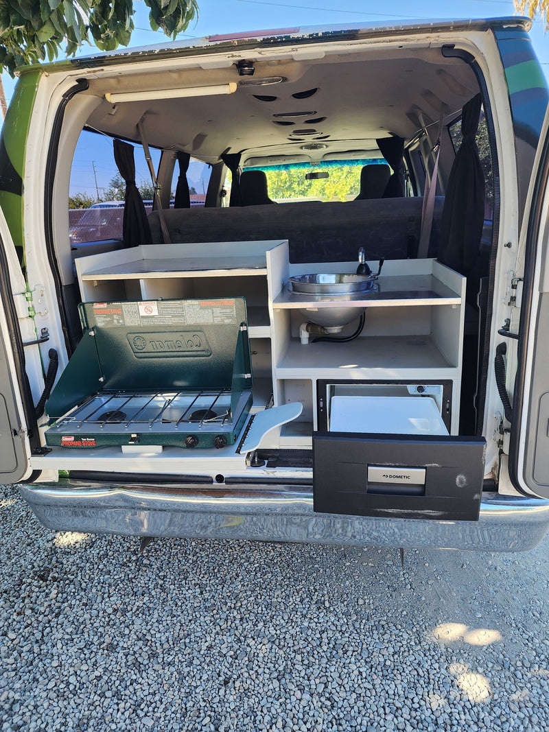 Explore with our RV rental camper van! Features a pull-out kitchen: Coleman stove, sink, and Dometic fridge. — photo 8
