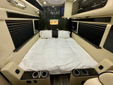 Interior of a luxury RV rental featuring a large bed with white bedding, TV, built-in cup holders, and pleated window blinds.