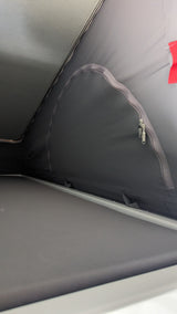 Interior view of an RV rental's pop-top sleeping area, featuring grey fabric walls, a zippered opening, and a support bar.