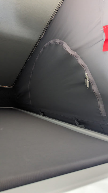 Interior view of an RV rental's pop-top sleeping area, featuring grey fabric walls, a zippered opening, and a support bar.