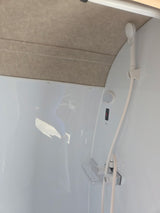 RV rental shower: A compact white interior featuring a handheld shower, faucet, and visible drain pump switch.