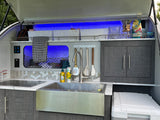 This RV rental's sleek outdoor kitchen includes a sink, Dometic stove, and ample, illuminated storage with blue accent lighting.