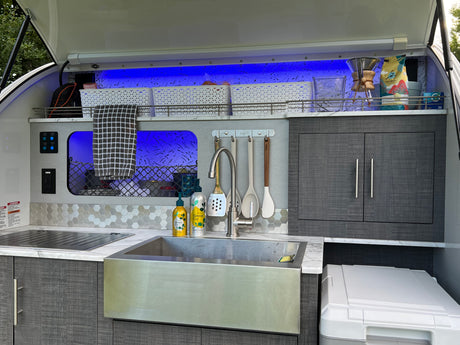 This RV rental's sleek outdoor kitchen includes a sink, Dometic stove, and ample, illuminated storage with blue accent lighting.